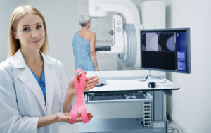 Breast cancer ribbon held by medical professional with mammogram machine in background.