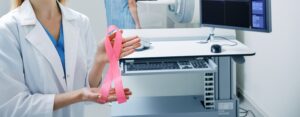 Breast cancer ribbon held by medical professional with mammogram machine in background.